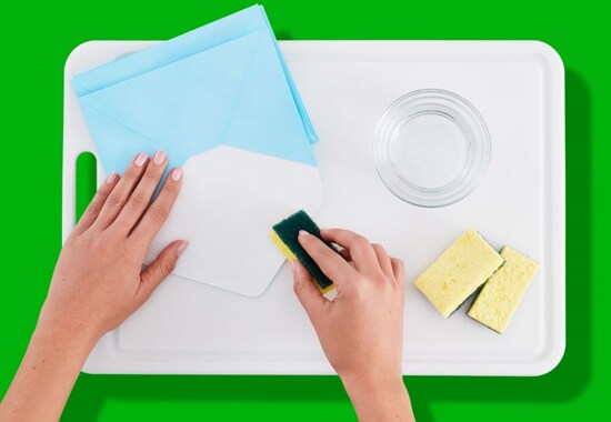 A person sealing an envelope with a wet Scotch-Brite® Sponge.
