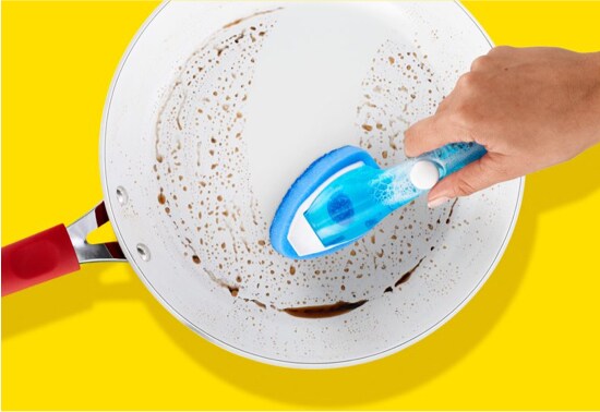 A person cleaning a dirty pan with a Scotch-Brite® Dishwand.
