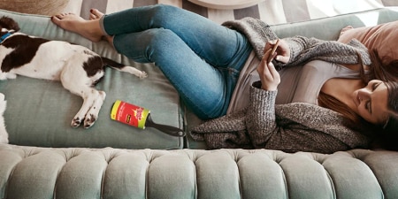 Woman reclining on a couch with her dog after removing pet hair with a lint roller.