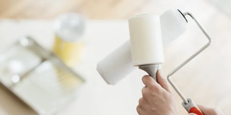 Person using a lint roller to clean a paint roller brush before painting.