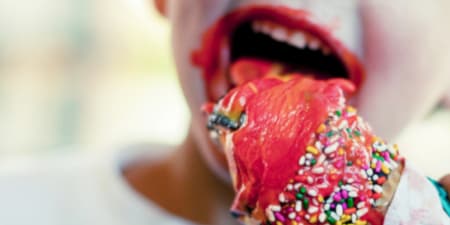 Child messily licking and eating a cherry ice cream cone with sprinkles.