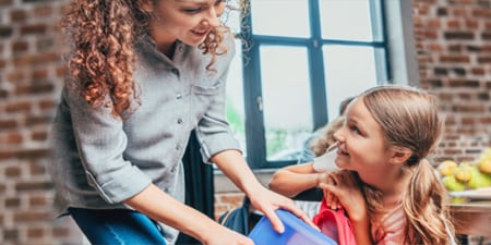 Mother helping her child pack her backpack for school.