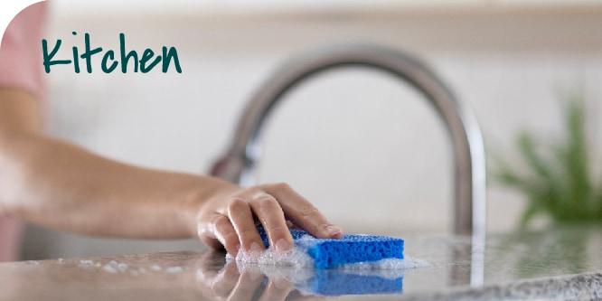 A person wiping a kitchen counter with a Non-Scratch Scrub Sponge.
