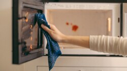 Person cleaning a microwave with a blue Scotch-Brite™ Brand dishcloth 
