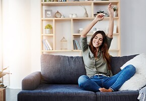 woman smiling on couch with hands over head