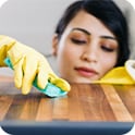 Person wearing yellow gloves cleaning a wooden surface with a sponge, focusing carefully.
