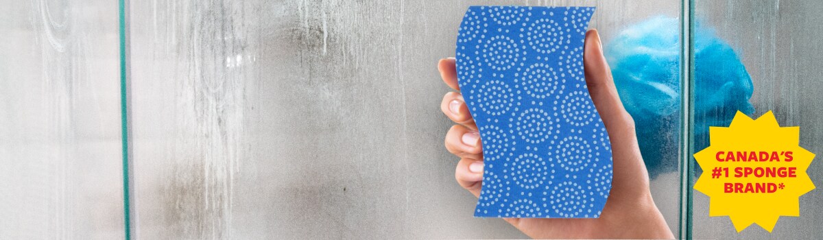 Woman holding a sponge about to clean a stand-up shower with clear glass or acryllic sides.
