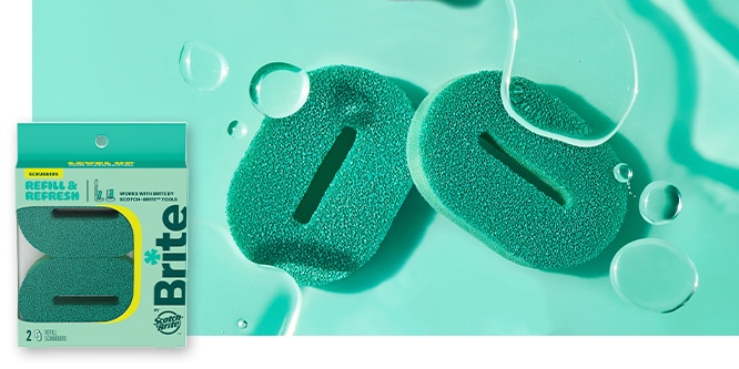 Two teal scrubbing sponges on a watery surface, with packaging visible in the corner.
