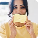Woman in a yellow shirt playfully holds a sponge to her face.
