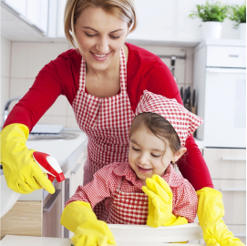 Une mère et sa jeune fille portant des gants de nettoyage en latex jaune, pulvérisant une solution nettoyante et nettoyant autour de l’évier de la cuisine.