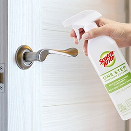 person spraying door handle with scotch brite one step cleaner and disinfectant