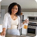 Person in a kitchen cleaning a counter with a spray bottle, wearing casual clothes, with a modern oven in the background.
