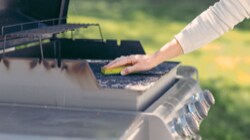 Person cleaning a stainless steel BBQ with a Scotch-Brite™ Brand sponge 

