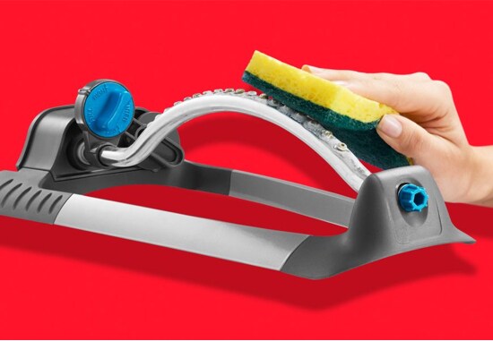 A person cleaning a lawn sprinkler with a Scotch-Brite® Heavy Duty Scrub Sponge.
