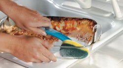 Person cleaning a dirty dish with a Scotch-Brite™ Brand dishwand
