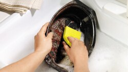 Person cleaning a roasting pan with a Scotch-Brite™ Brand sponge 
